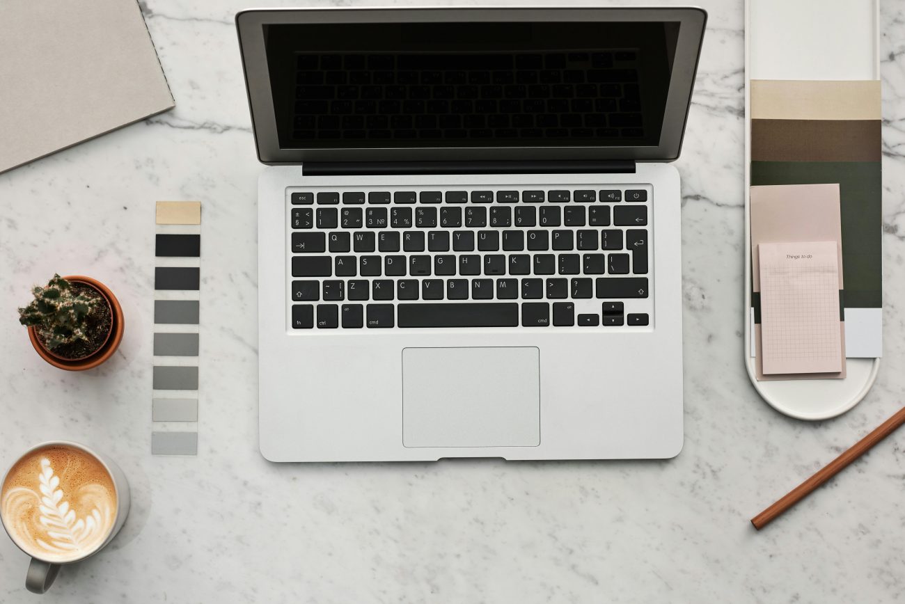 Top view of a stylish workspace featuring a laptop, latte, cactus, and color swatches on a marble surface.